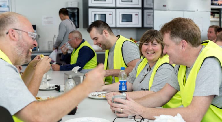 Siemens - a group of colleagues in high-vis vests eating lunch and talking together